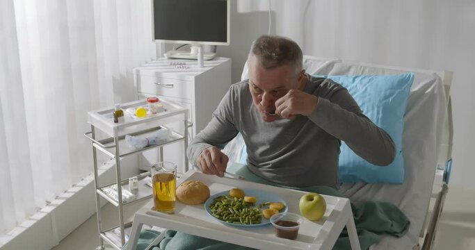 Aged male patient eating breakfast on tray in hospital bed