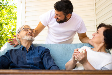 Happy senior couple laughing with adult brunette bearded son enjoying weekend family time at home together, having pleasant conversation, hugging them with love and care.Generation and people concept