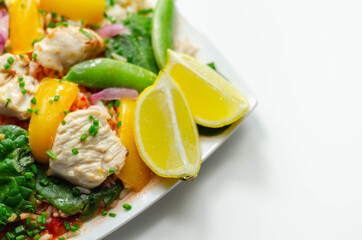 Cooked chicken breast pieces with peppers, sugar snap peas, and baby leaf spinach in a spicy sweet and sour sauce with fragrant rice