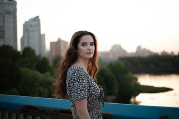 Portrait photo of a young and beautiful woman. Summer time of the year. Happy woman stands on the bridge overlooking the city
