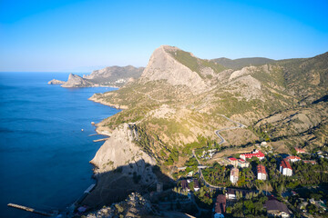 Obraz premium The rocky coast of the sea with a settlement and a mountain road. Shooting from a drone.