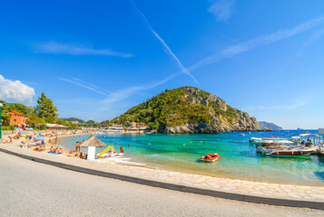 Fototapeta na wymiar A sunny day at Palaiokastritsa beach as tourists sunbathe and swim in the sea on the island of Corfu, Greece.