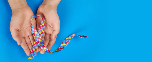 World Autism awareness day. Autistic boy hands holding puzzle pattern ribbon on blue background