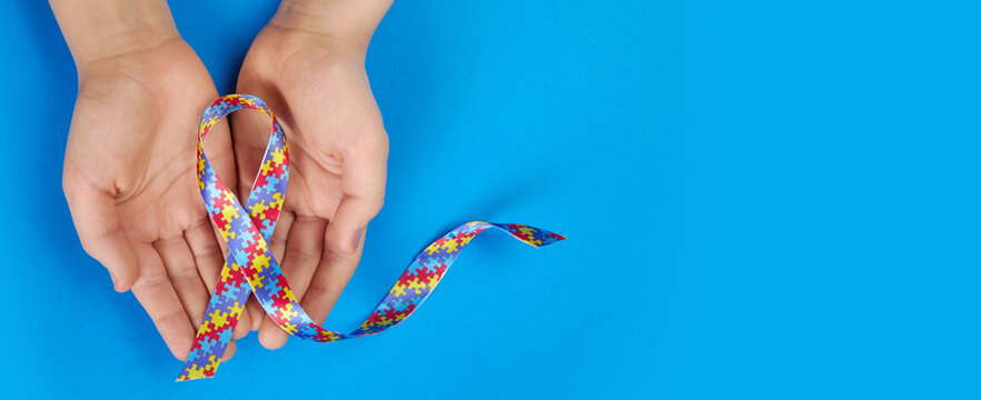 World Autism awareness day. Autistic boy hands holding puzzle pattern ribbon on blue background