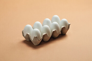 A tray of white fresh  eggs on beige background. Eco-friendly egg production. Organic chicken eggs.
