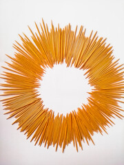 Close-up of wooden toothpicks arranged in a circle in the shape of the sun, on a white background.