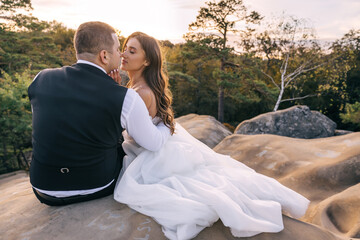 The wedding couple sits and hugs against the background of a stone river. Rear view on the background of beautiful nature.