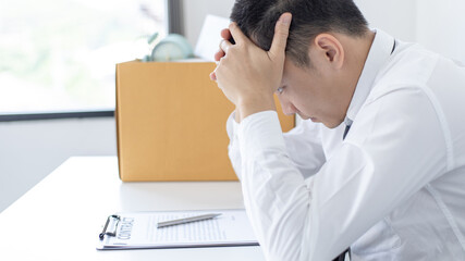 Naklejka premium Businessman held his temple with his hand and had a brown document box beside it, Businessmen hand in resignation papers and packing office supplies in boxes with regret or disappointment.