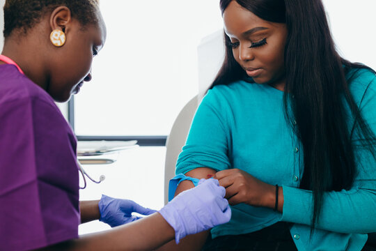 Black nurse collects blood sample from female patient at doctors office