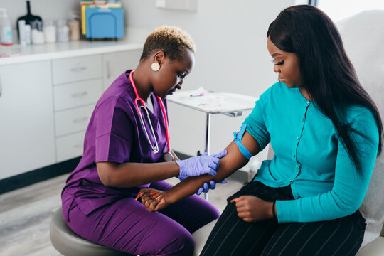 Black nurse collects blood sample from female patient at doctors office