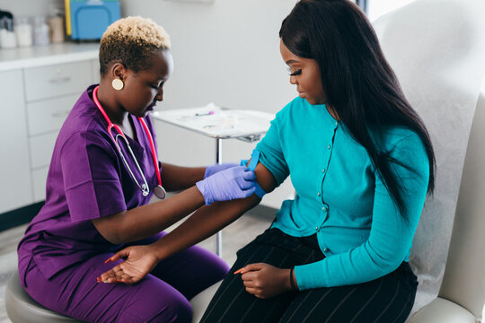 Black nurse collects blood sample from female patient at doctors office