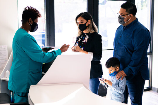 Black nurse reviewing medical forms with Latino family at doctor office