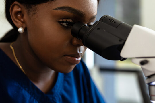 Black female medical professional in laboratory looking through microscope