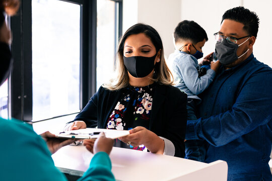 Nurse handing medical forms to Latino family for check in at doctor office