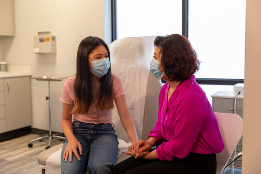 Mother And Daughter Waits To See Doctor In Medical Exam Room With Mask