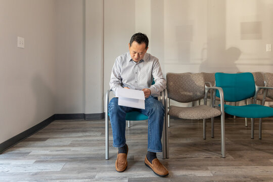 Asian man filling out patient forms at doctors office waiting area