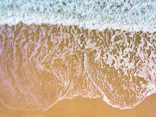Aerial shot of the foam of the sea waves with orange sand and green water