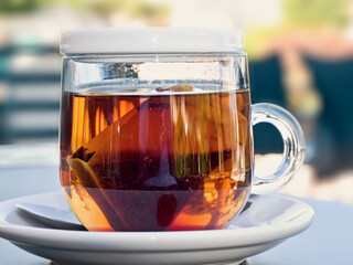 A tea glass filled with freshly brewed tea with a tea bag, photographed against the light and close-up. Soft bookeh in the background.