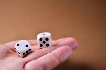 White dice lie in the palm of your hand close up on a brown background with a copy space. High quality photo