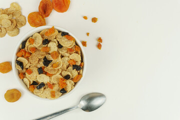 A bowl of cornflakes with dried apricots and prunes, a spoon. White background