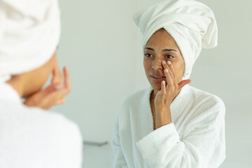 Mixed race woman wearing bathrobe and cleansing face mask in bathroom