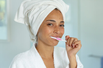 Mixed race woman wearing bathrobe and brushing teeth in bathroom