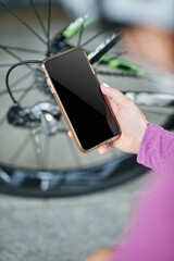 Close up shot of hand of female cyclist holding smartphone while checking her bicycle mechanisms, sprocket and chain on a mountain bike outdoors on a daytime