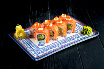 Fresh, Japanese sushi rolls with cucumber, caviar and salmon, served in a plate with wasabi and ginger on a dark background. Japanese kitchen. Red dragon roll in sesame