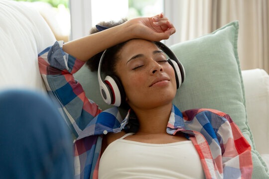 Mixed race woman lying on couch listening to music with headphones at home