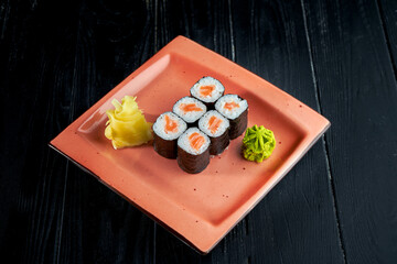 Appetizing Japanese sushi - maki with salmon served in a plate with ginger and wasabi on a black wood background. Japanese cuisine