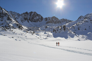 two skiers hiking a trail through the snowy mountains during the winter on a sunny day