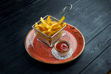 The standard side dish is French fries, served in a basket in a plate with red sauce. Black wood background. Fast food
