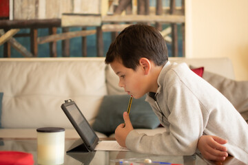 Fototapeta premium Portrait of a boy doing his homework at the laptop, isolated in the living room