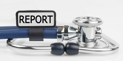 On the white surface lies a stethoscope with a plate with the inscription - REPORT