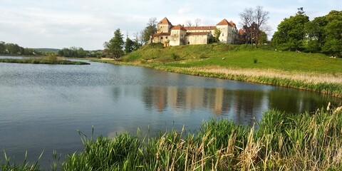 Fototapeta na wymiar Amazing panorama of Svirzh medieval castle, reflected in water of nearby lake under high blue sky with clouds