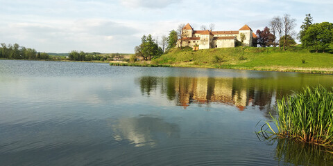 Amazing panorama of Svirzh medieval castle, reflected in water of nearby lake under high blue sky with clouds