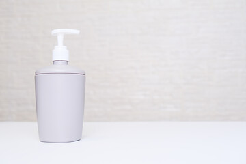 A gray liquid soap dispencer, bottle against white background in a bathroom with copy space