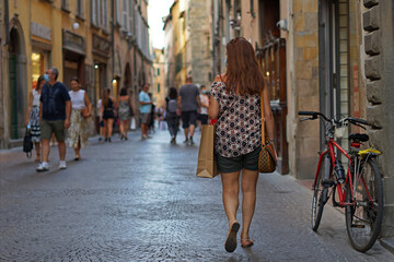 Elegant woman strolls through the shopping street. Lady with red hair and paper bag goes shopping wearing an anti covid mask.