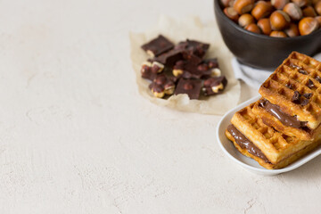 Waffles with chocolate-nut spread, a bowl of nuts, pieces of chocolate on the table. space for text with copy space
