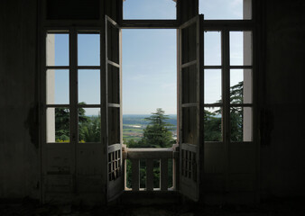 Large window overlooking a green valley.
Escape from an abandoned house. French window ruined by time.