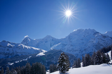Beautiful winter landscape with star shaped sun at Mürren, Switzerland with Mountain peaks Eiger, Mönch and Jungfrau in the background.