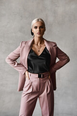 A fashionable young woman with blond hair and perfect makeup in a black blouse and an elegant suit posing in the studio