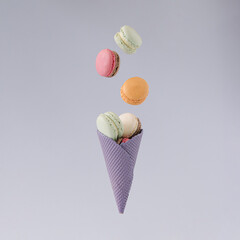 Pastel purple cone with flying sweet macarons  against gray background. minimal concept.