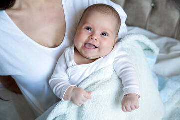 The baby is happy and laughing. The child is 3 months old in the mother's arms. Mom and beautiful daughter on a white background 