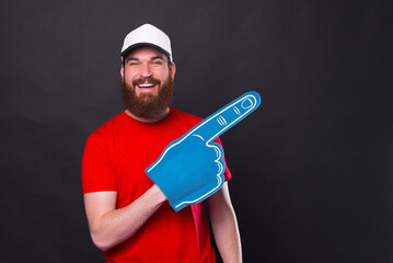 Fototapeta Cheerful portrait of young bearded man in red t-shirt pointing away with fan foam glove obraz
