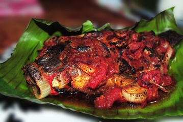 Thick slieces of chicken barbeque with onion rings bathed in sauces, served in a banana leaf