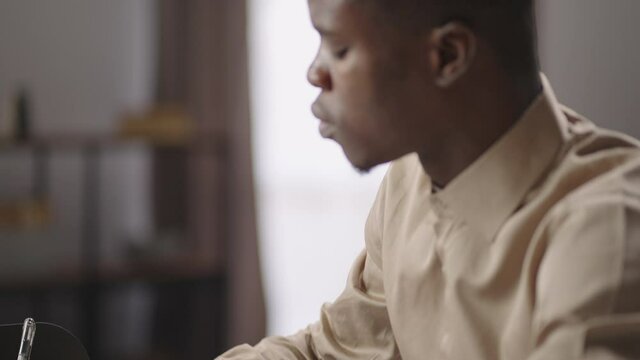 young black male writer or journalist is working at home, writing rough draft by pen on paper, sitting at table with laptop
