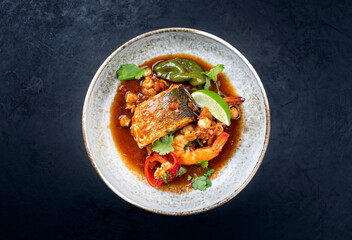 Modern style traditional Mexican seafood pozole soup with fish, king prawns and hominy in a clear sauce served as top view in design bowl