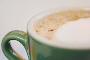 Coffee in green cappuccino ceramic cup with frothy foam, latte capuccino mug closeup. Hot coffee...