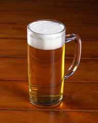 One glass mug with lager or porter is delicious frothy beer on a wooden tabletop a sunny day.